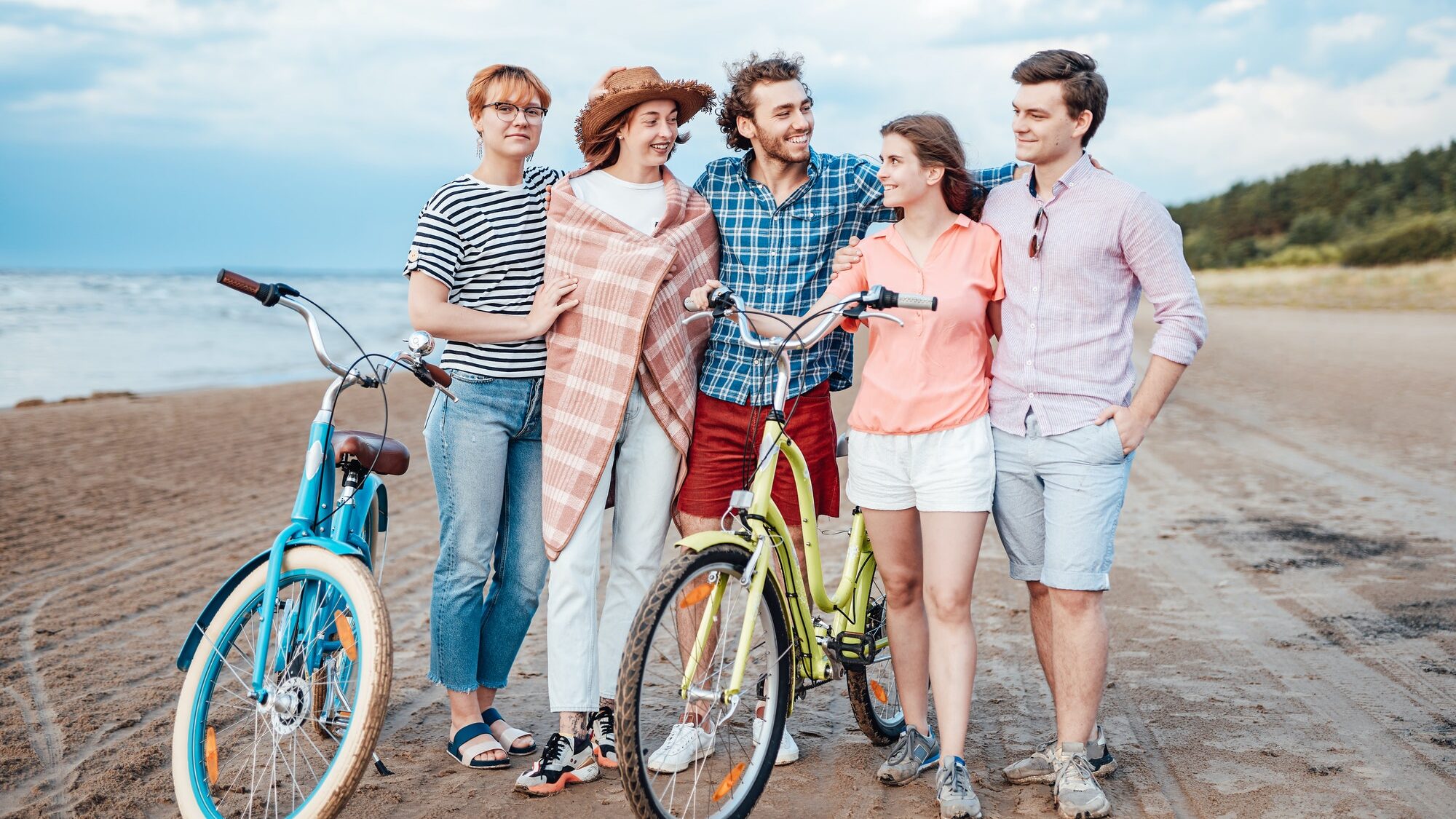 Five friends on the beach with their bicycles, hugging each other